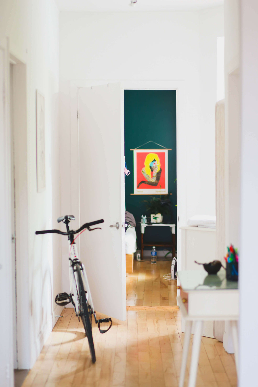 A hallway with a bicycle leaning against the wall and a colorful artwork hanging on the back wall.