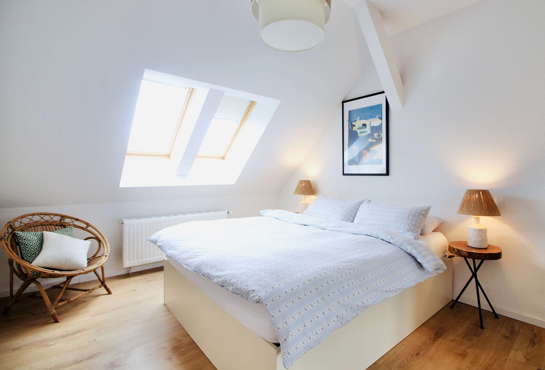 Cozy attic bedroom with sloped ceiling, large windows, and warm lighting featuring a comfortable bed and stylish decor.