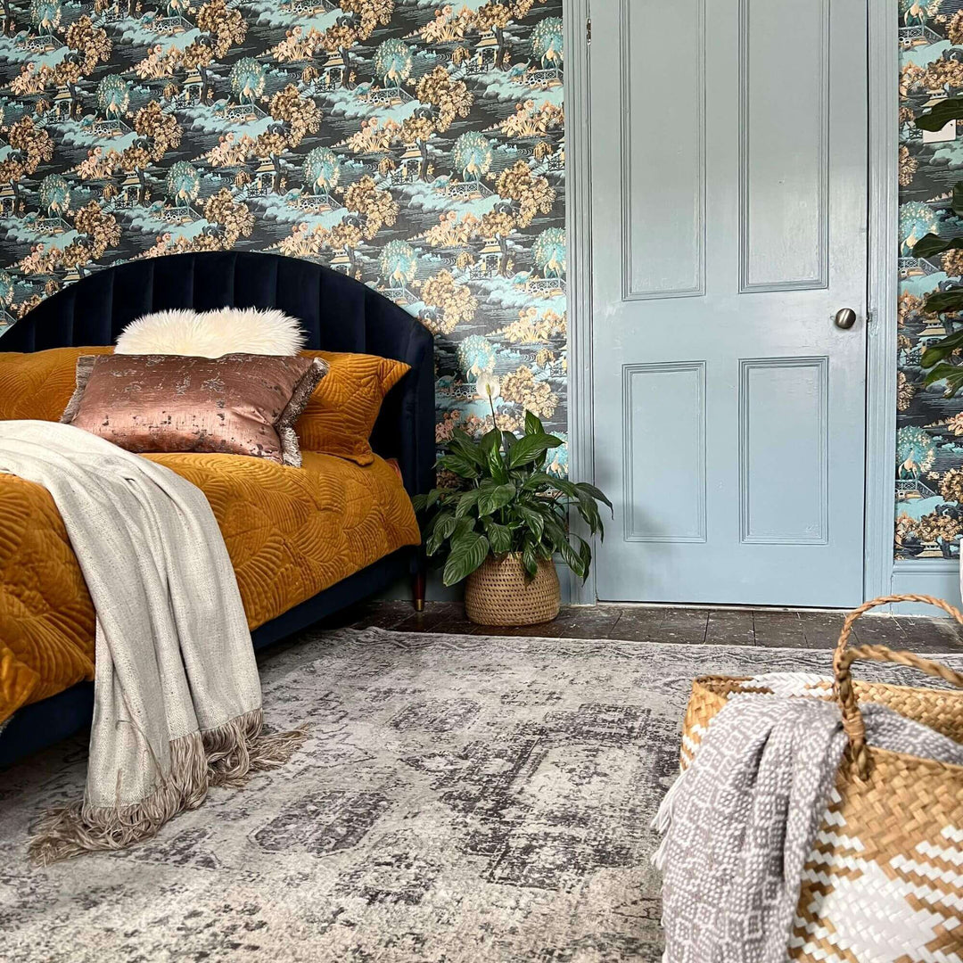 Cozy bedroom with blue wallpaper, a dark bed, a plush blanket, and indoor plants, creating a stylish and inviting atmosphere.