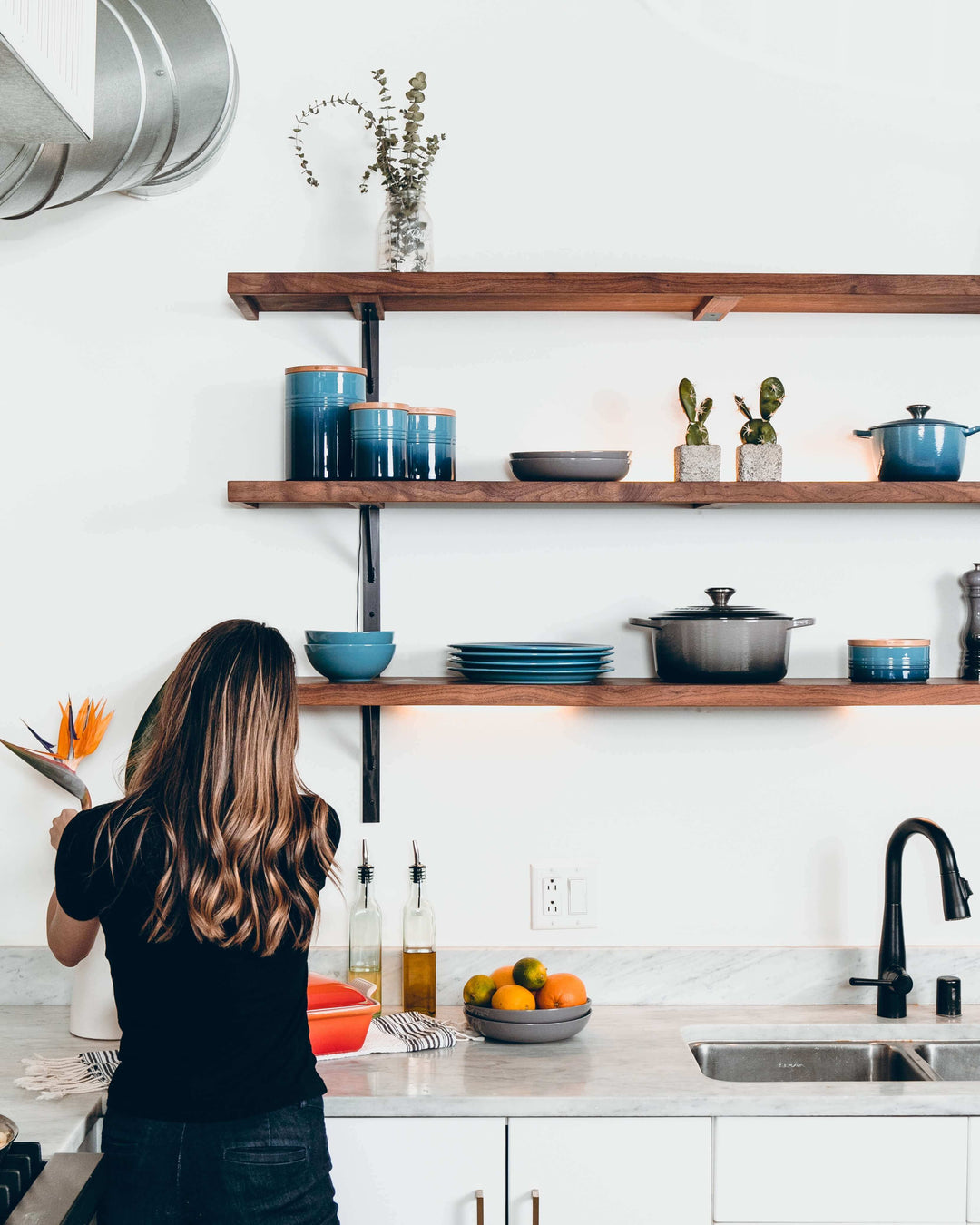 Modern kitchen with open shelves, blue dishes, and a person preparing food.