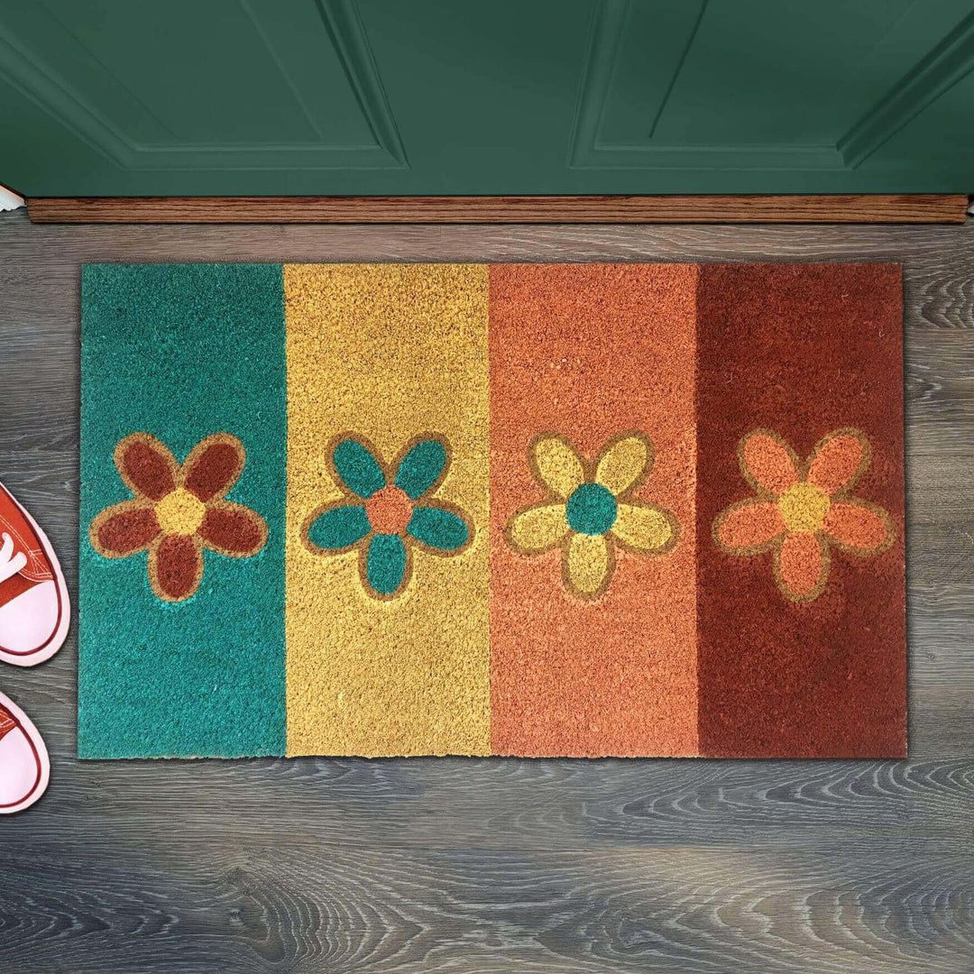 Colorful flower-patterned doormat with blue, yellow, orange, and brown sections beside pink shoes.
