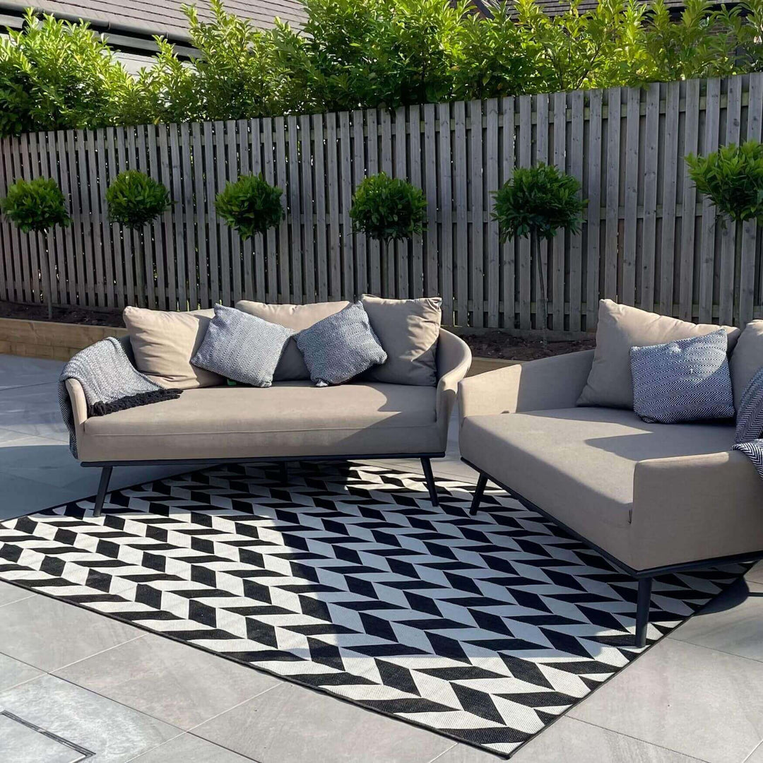 Modern outdoor seating arrangement with stylish cushions on a geometric rug and lush greenery in the background.