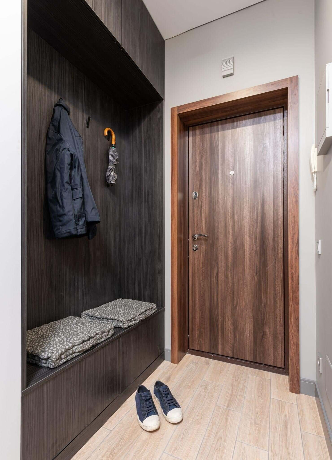 Modern hallway with a wooden door, coat rack, and shoes, showcasing stylish interior design.