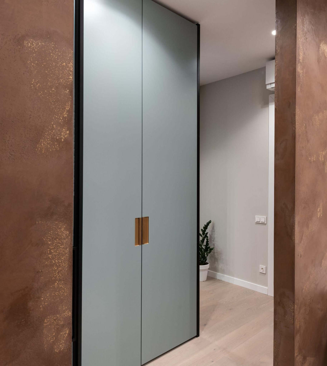 Modern sliding glass wardrobe with gold handles in a stylish interior hallway.