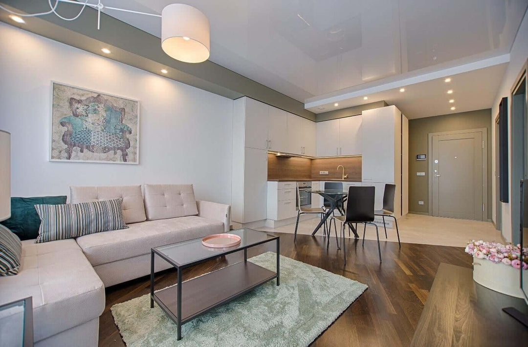Modern living room with a beige sofa, stylish decor, and kitchen area, featuring warm lighting and a cozy atmosphere.