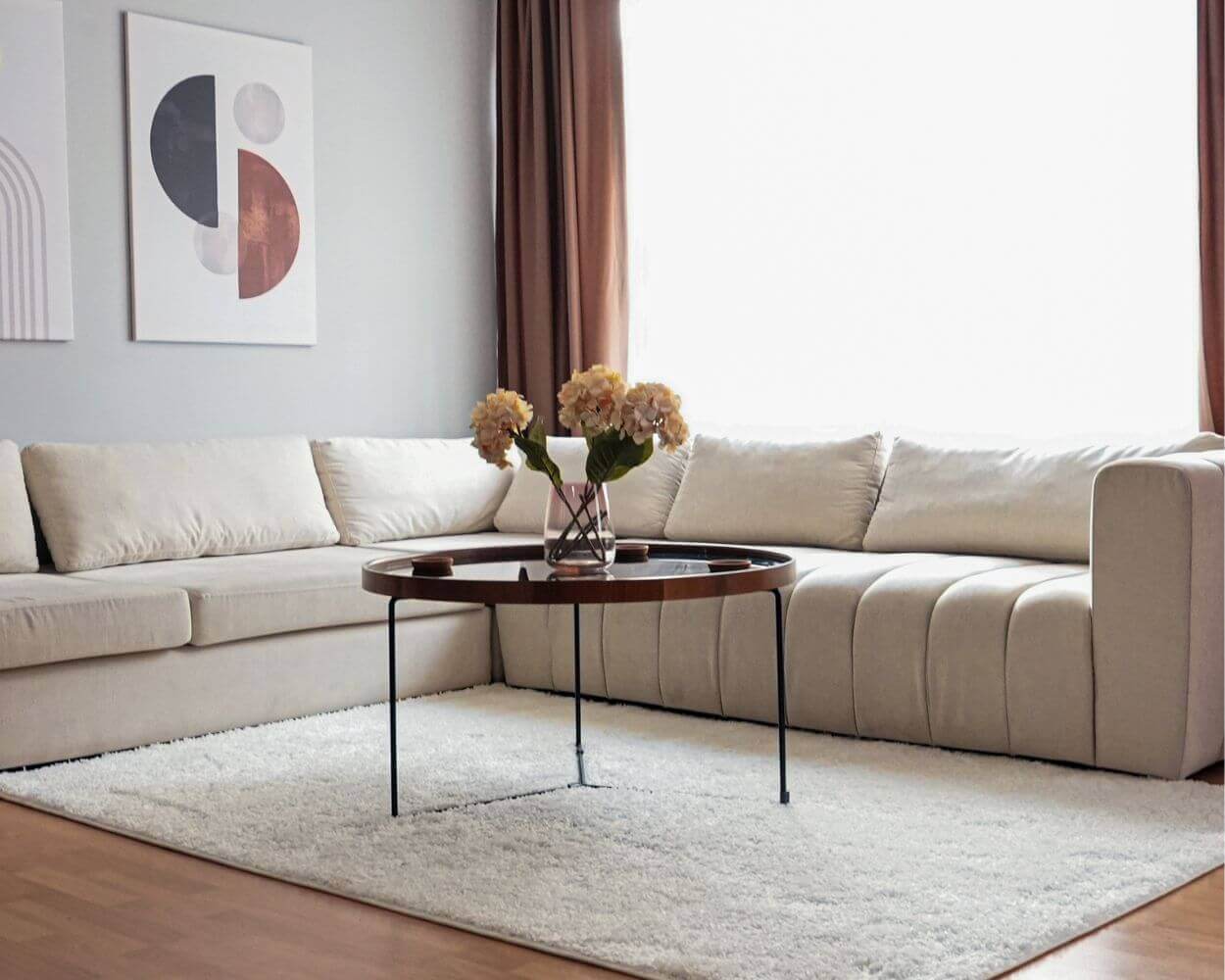 Modern living room featuring a light beige sectional sofa, round coffee table, and decorative flowers.