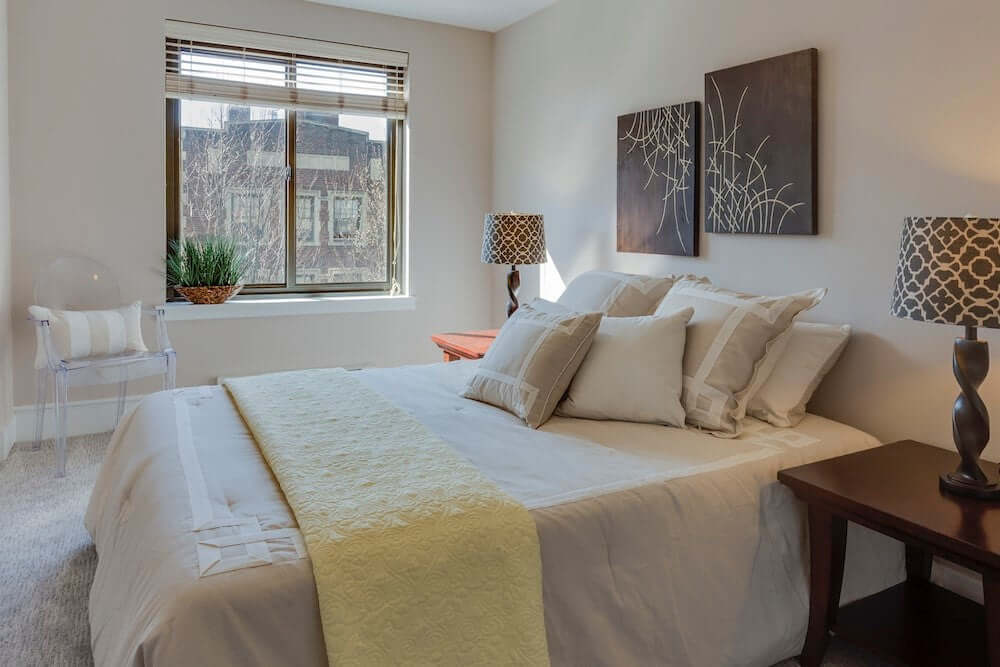 Cozy modern bedroom featuring a comfortable bed, decorative pillows, and stylish lamps near a window.