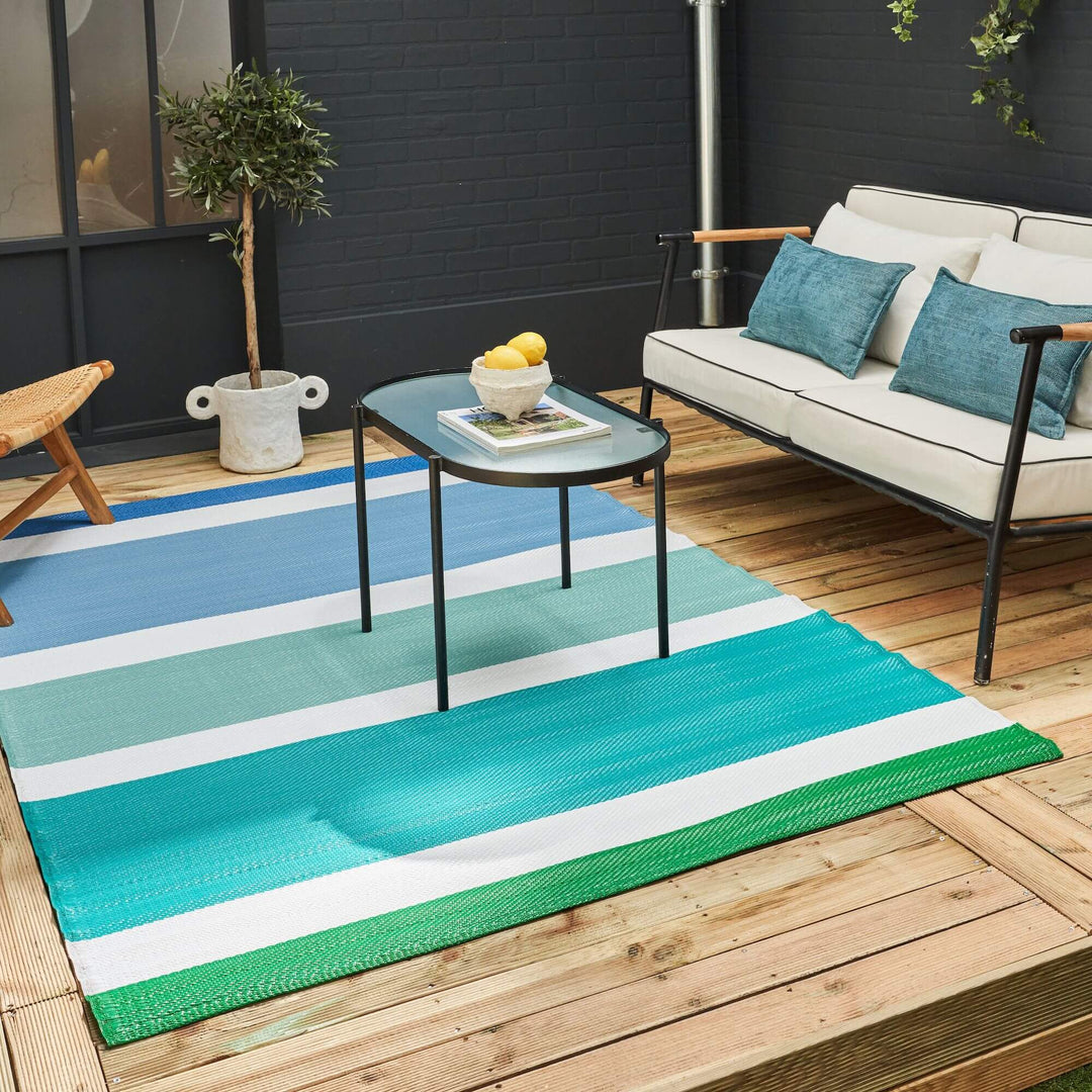 Vibrant striped geometric blue outdoor rug on patio with sofa and table, enhancing modern outdoor decor.