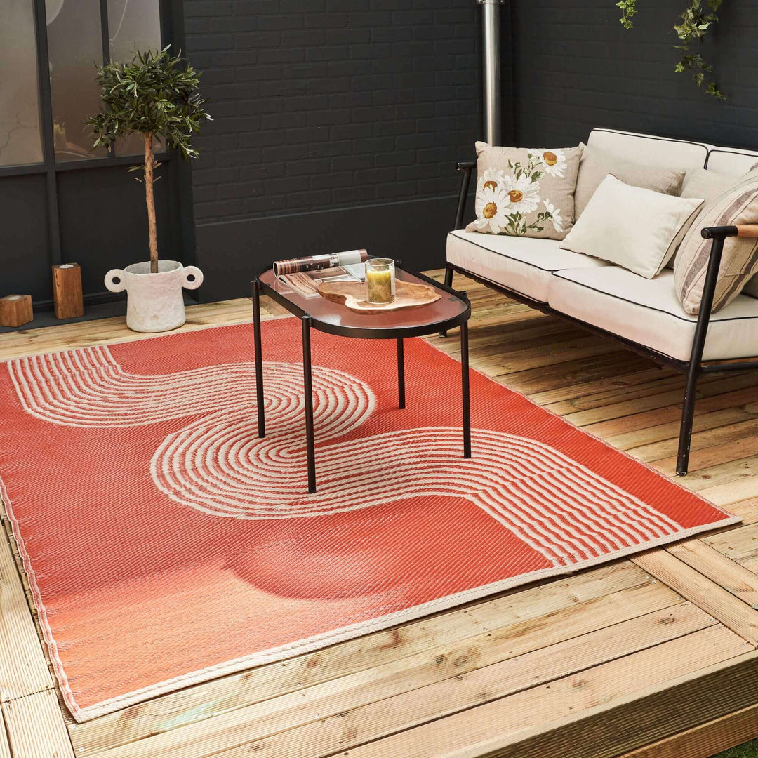 Terra and beige urban outdoor rug on a wooden deck with modern sofa and table, showcasing geometric patterns and contemporary design.