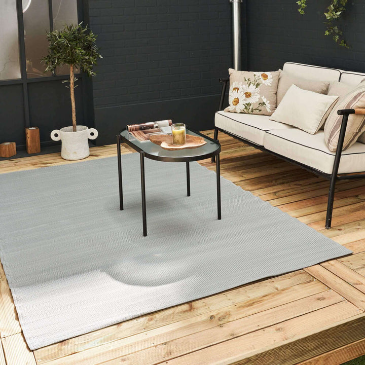 Sleek grey outdoor rug on patio with modern table and sofa, enhancing the elegant outdoor decor setting.