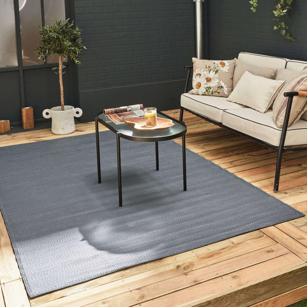 Urban outdoor rug in anthracite with geometric design on a wooden deck, paired with modern patio furniture and décor.