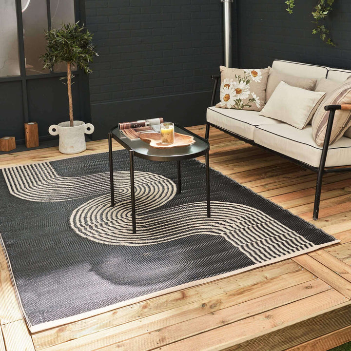 Black and beige geometric outdoor rug on a wooden deck with modern patio furniture.