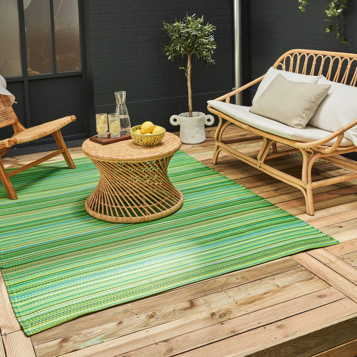 Vibrant green Rainbow Outdoor Rug in stylish patio seating area with wicker furniture and plants.