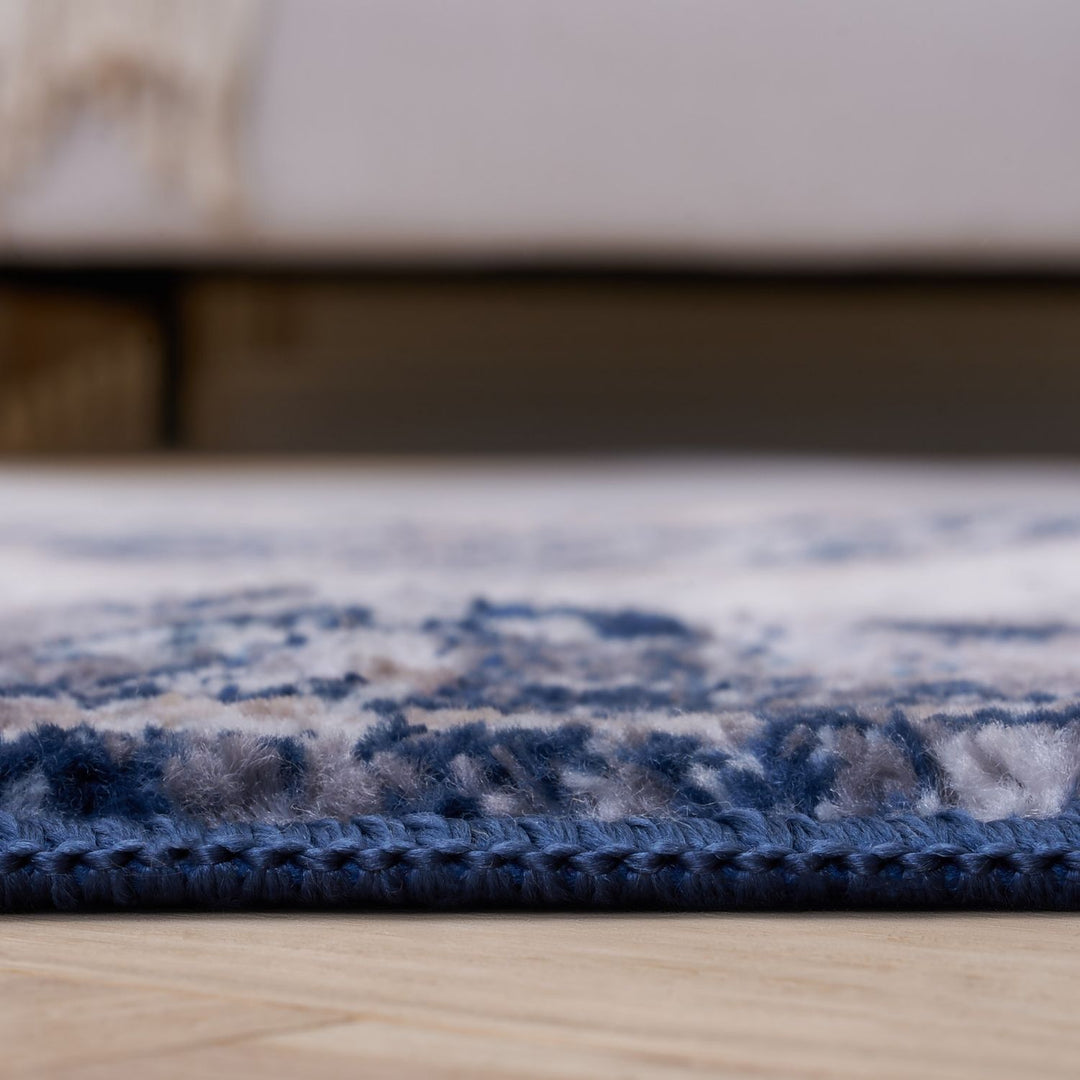 Close-up of a blue and beige patterned rug on a wooden floor.