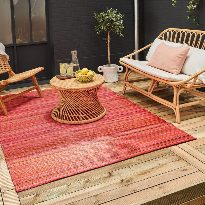 Vibrant rainbow outdoor rug with colorful geometric stripes on a stylish patio setting with wicker furniture.