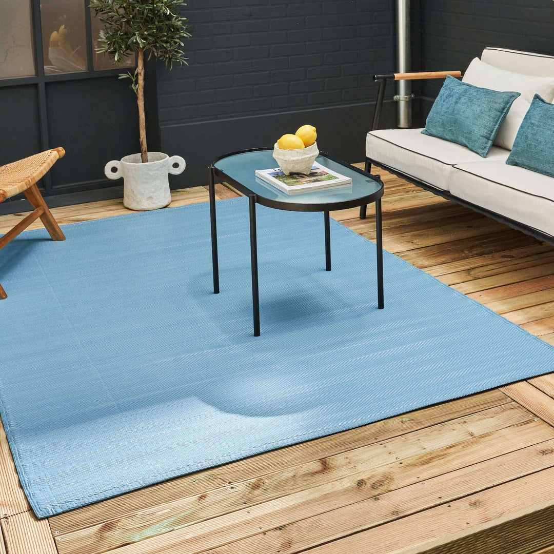 Blue outdoor rug on a wooden deck, surrounded by modern outdoor furniture.