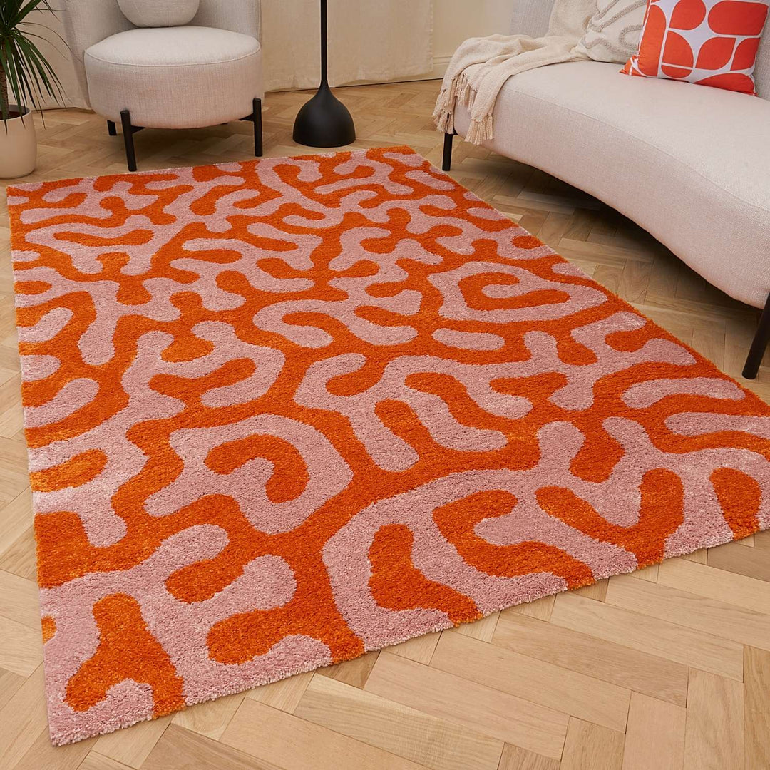 Orange and pink patterned rug on a wooden floor with a sofa and chair in the background.