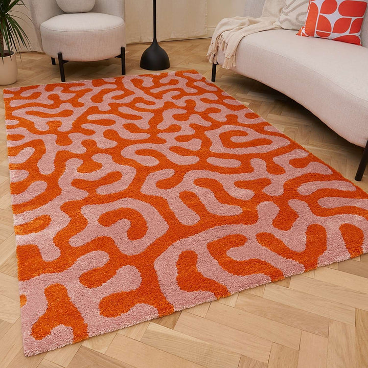 Orange and pink patterned rug on a wooden floor with a sofa and chair in the background.