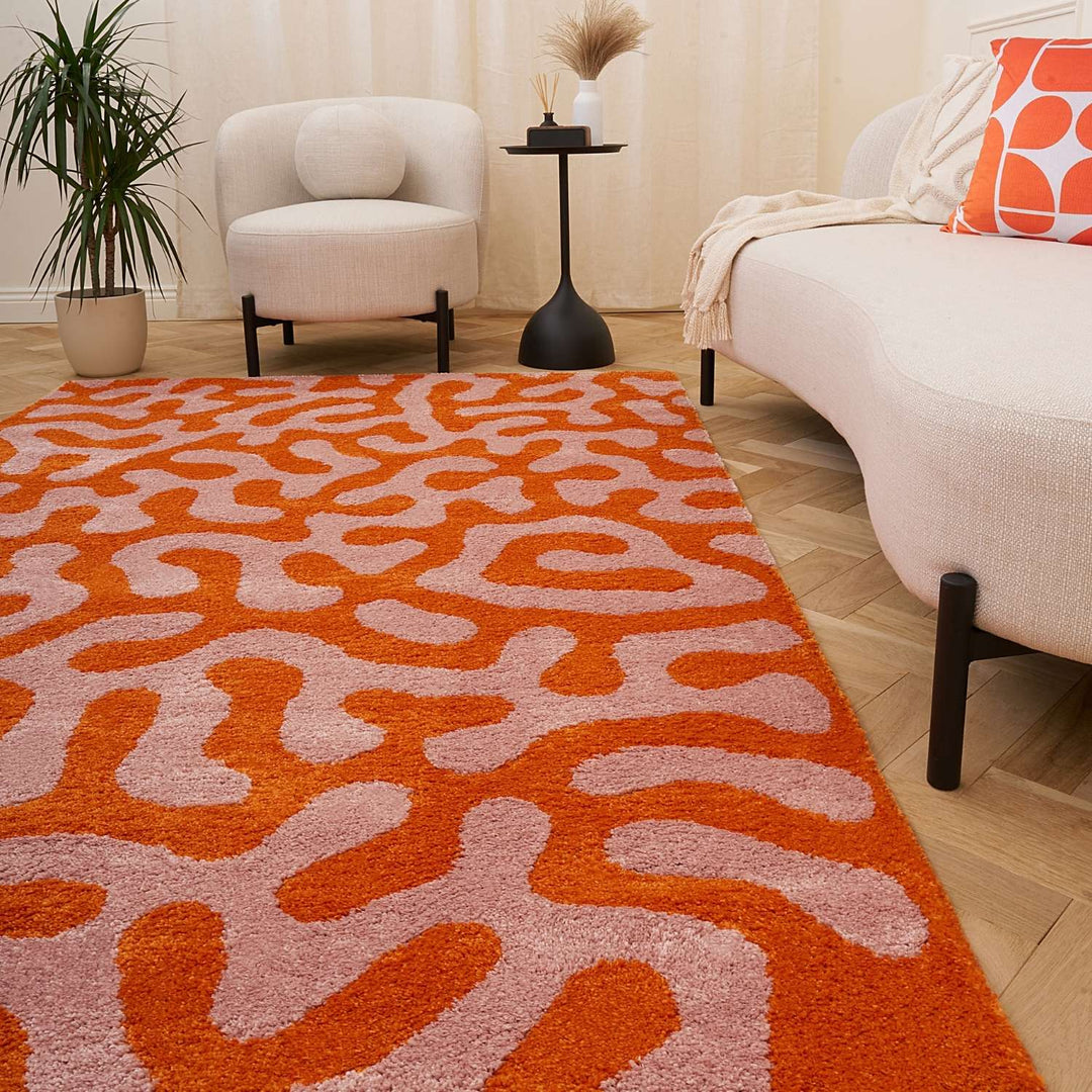 Living room with a patterned orange and pink rug, white armchair, and beige sofa.