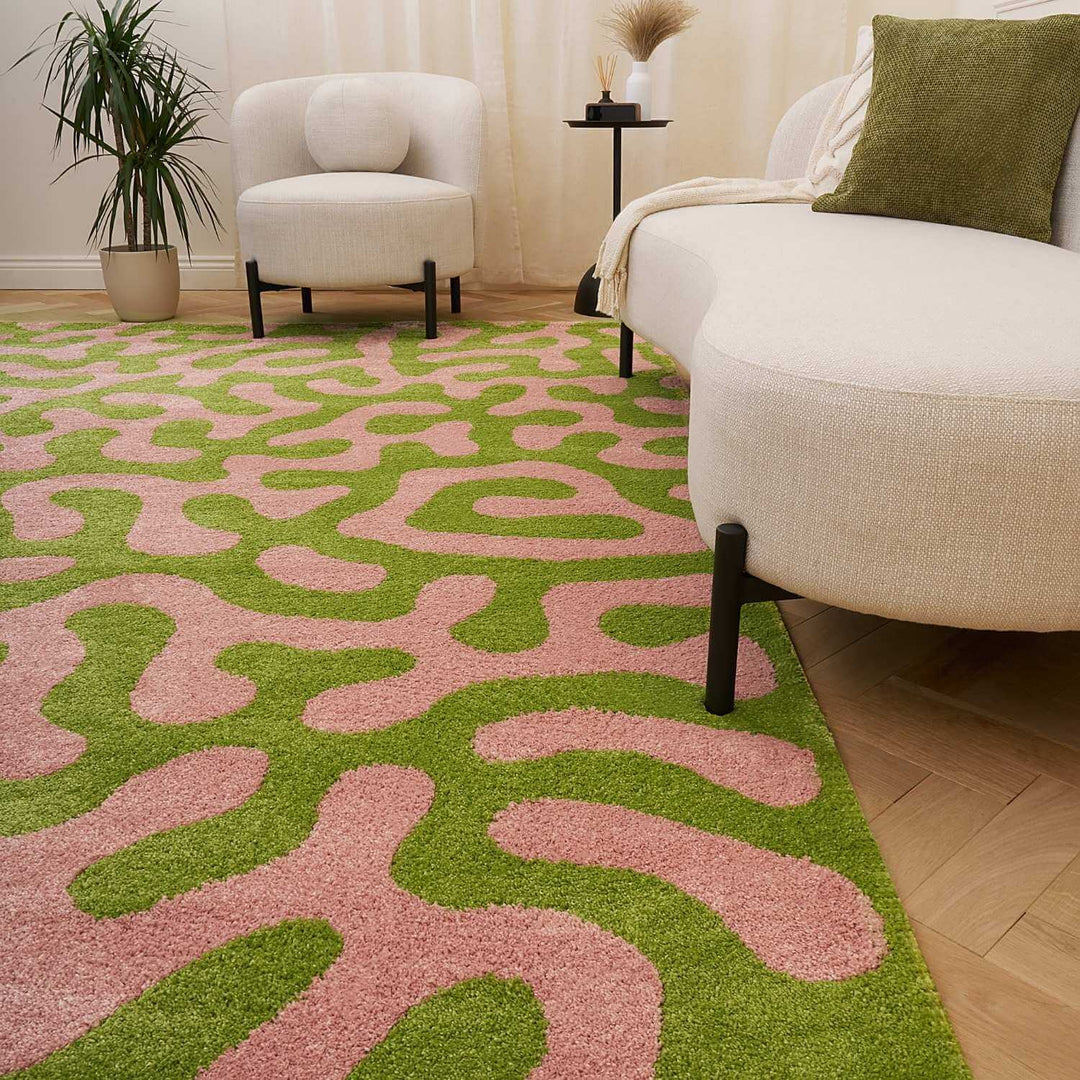 Living room with a green and pink patterned rug, beige sofa, and white armchair.