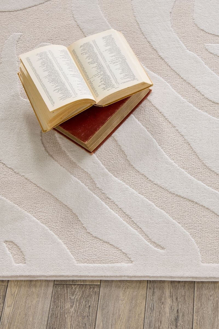 Abstract geometric rug in cream shades with books on top, showcasing modern design and soft texture.