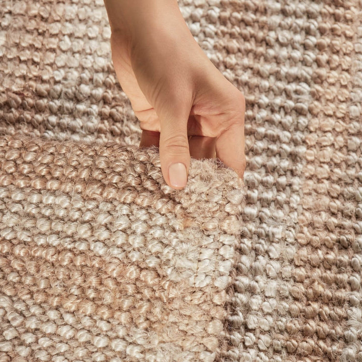 Close-up of a hand touching a textured beige carpet