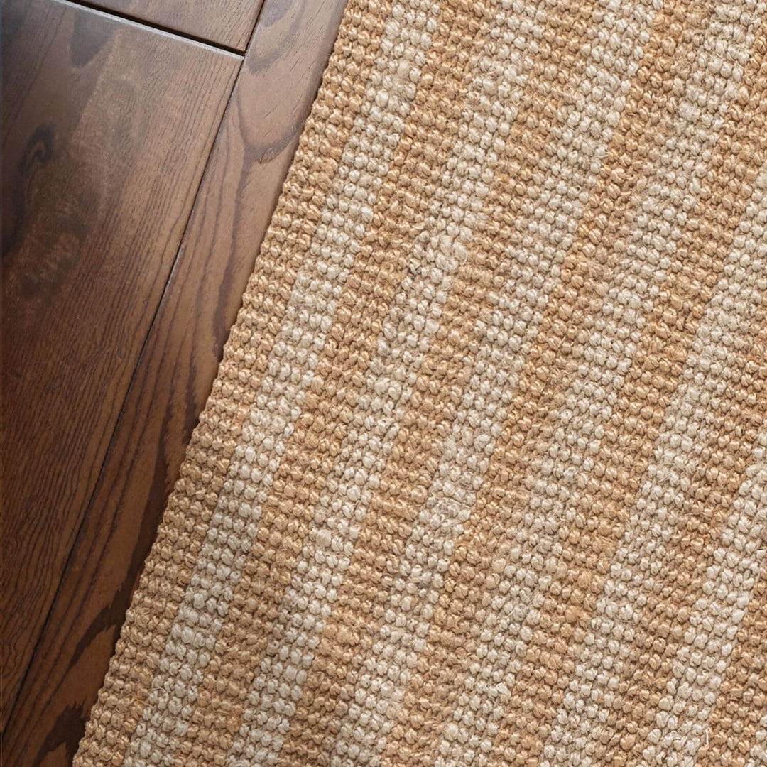 Close-up of a textured beige and brown rug on a wooden floor.