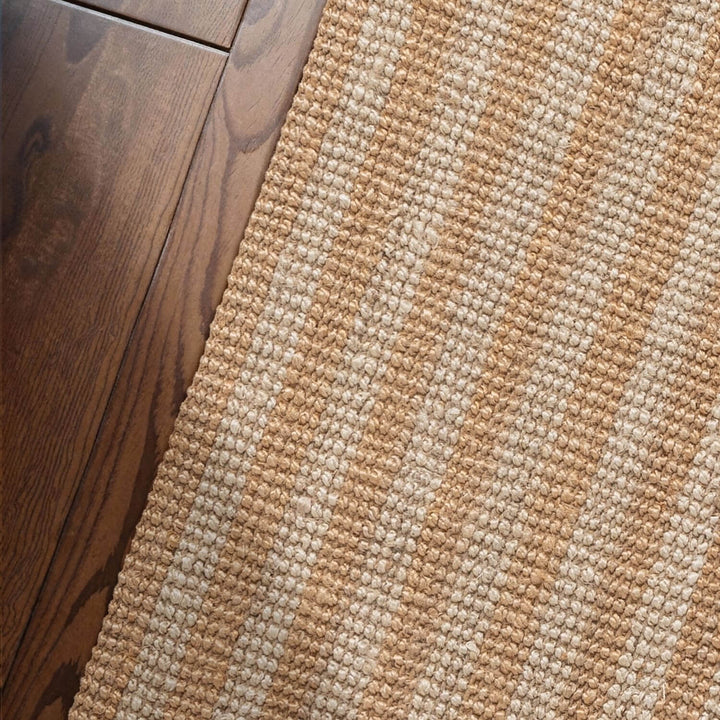 Close-up of a textured beige and brown rug on a wooden floor.