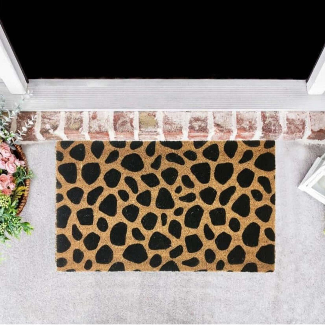 Doormat with leopard print pattern on a gray floor outside a house.