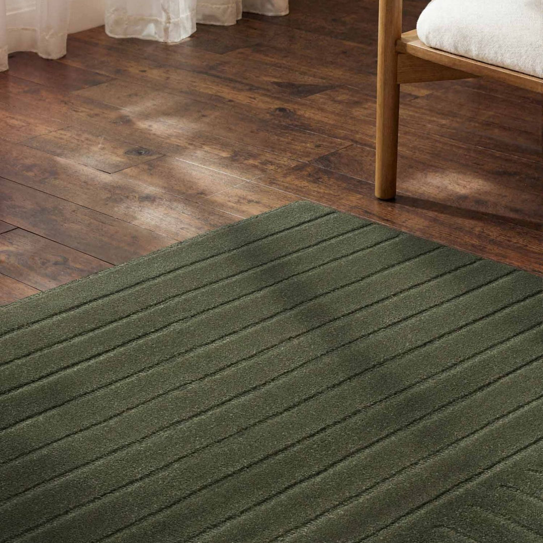 Green rug on a wooden floor with a bed partially visible