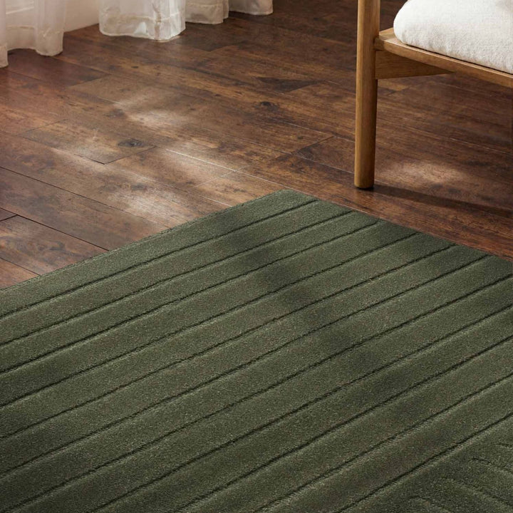 Green rug on a wooden floor with a bed partially visible