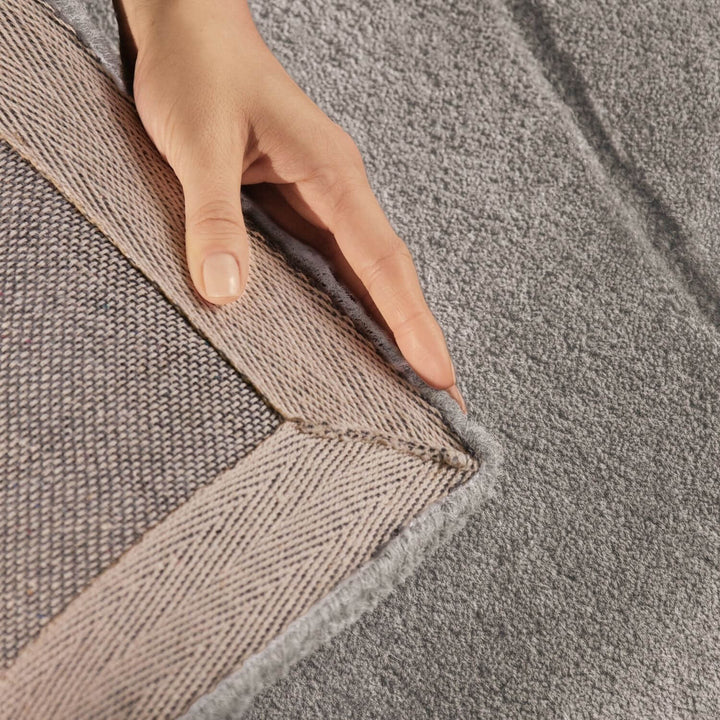 Close-up of a hand touching the edge of a textured gray rug.