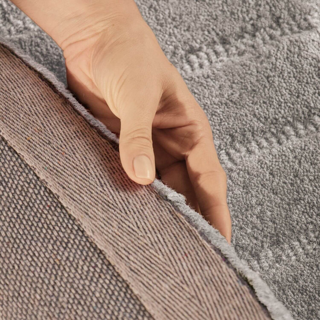 Hand touching the edge of two different textured carpets.