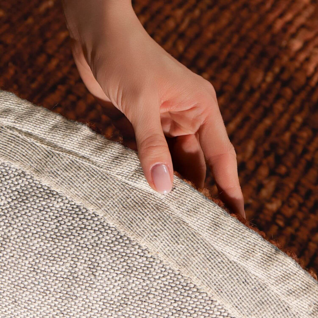 Hand touching the edge of two textured fabrics, one brown and one gray.