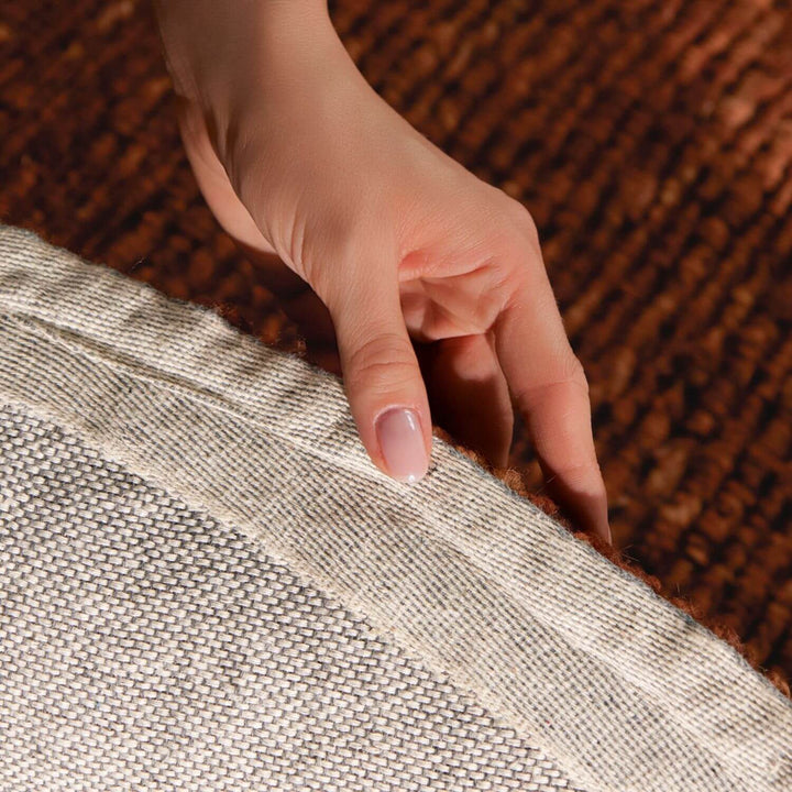 Hand touching the edge of two textured fabrics, one brown and one gray.