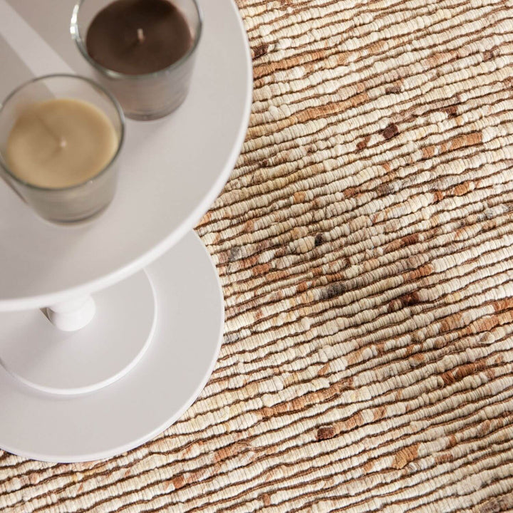 Close-up of a textured rug with a white candle holder and candles on a textured surface.