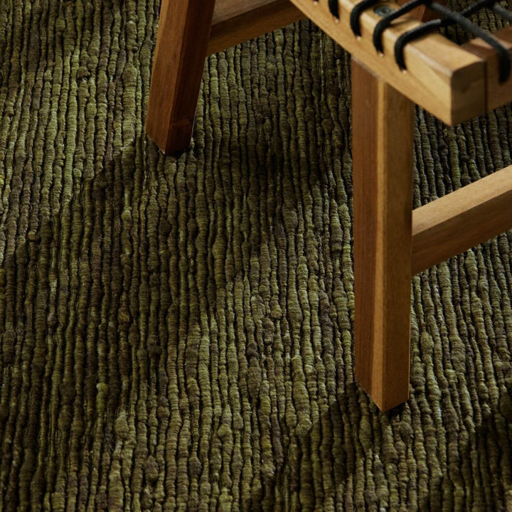 Close-up of a textured green carpet with a wooden chair leg.