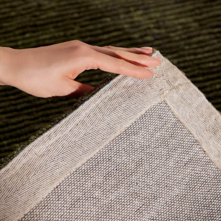Hand touching a textured gray rug with a blurred green background