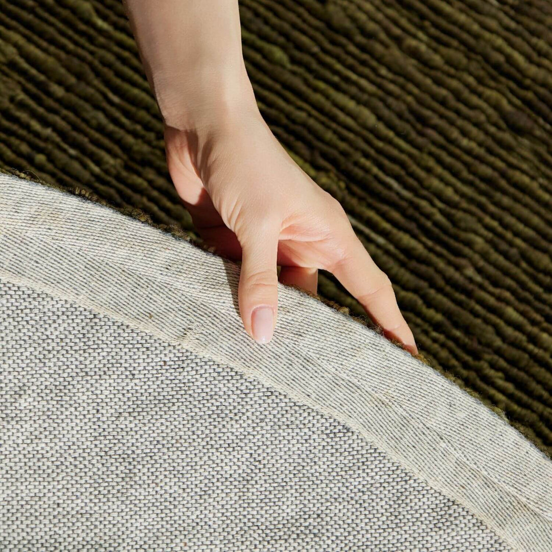 Hand touching the edge of a gray rug on a textured brown floor