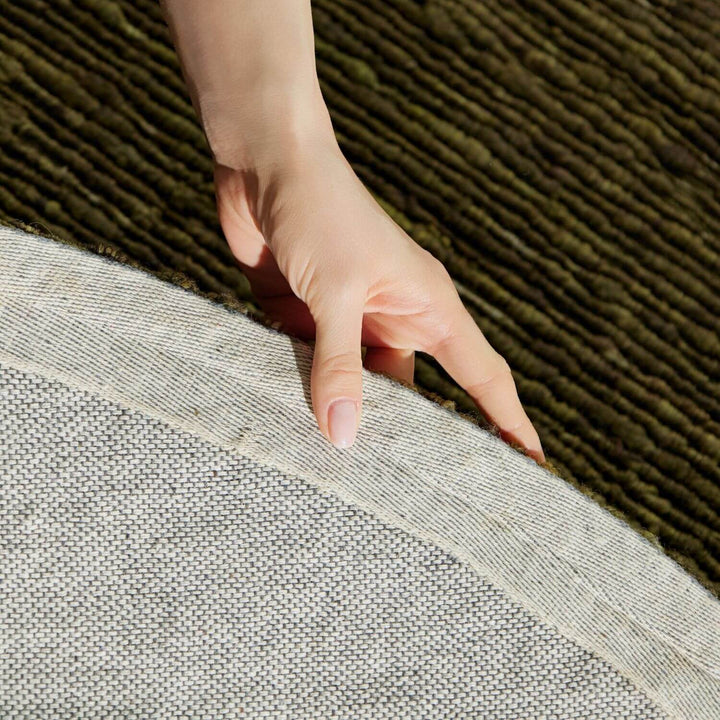 Hand touching the edge of a gray rug on a textured brown floor