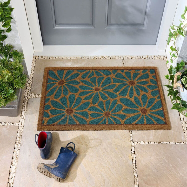 Decorative doormat with floral pattern on a stone patio in front of a gray door.