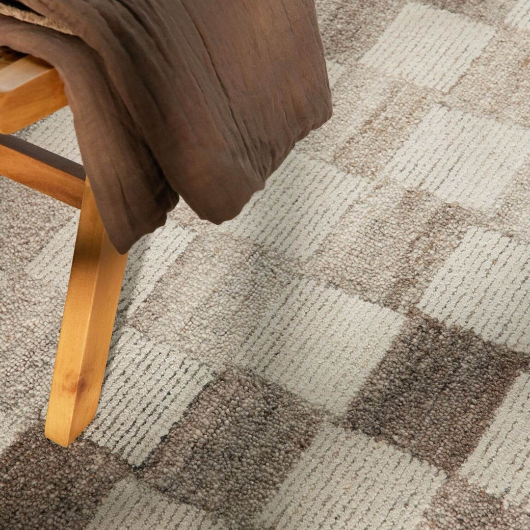 Close-up of a checkered patterned carpet with a wooden chair leg and brown fabric.