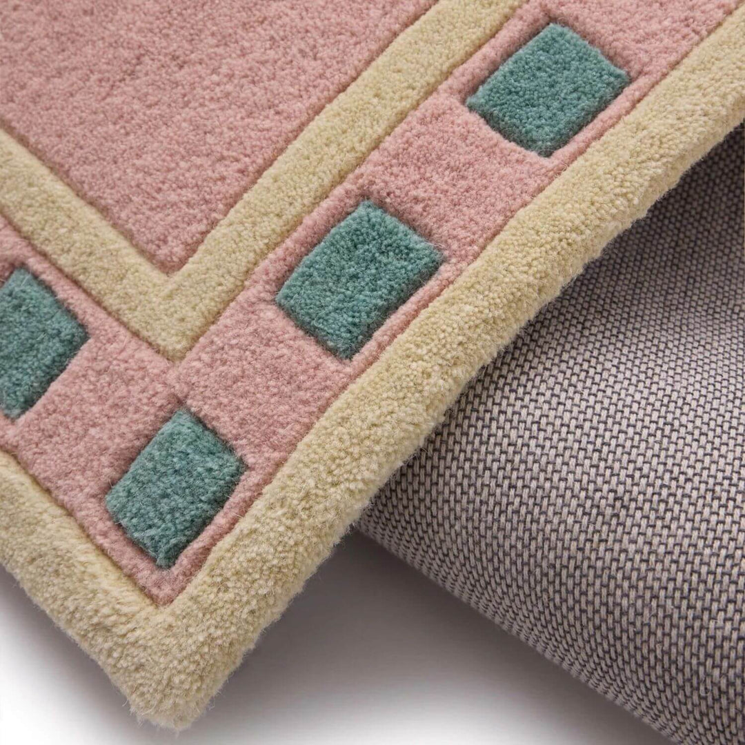 Close-up of a geometric-patterned rug with pink, green, and beige colors.
