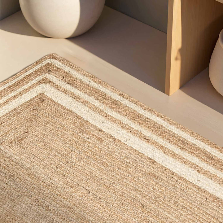Close-up of a woven jute rug with a geometric pattern on a neutral background.