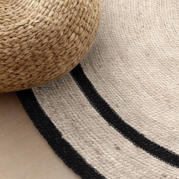 Close-up of a textured rug with black stripes and a woven ottoman.