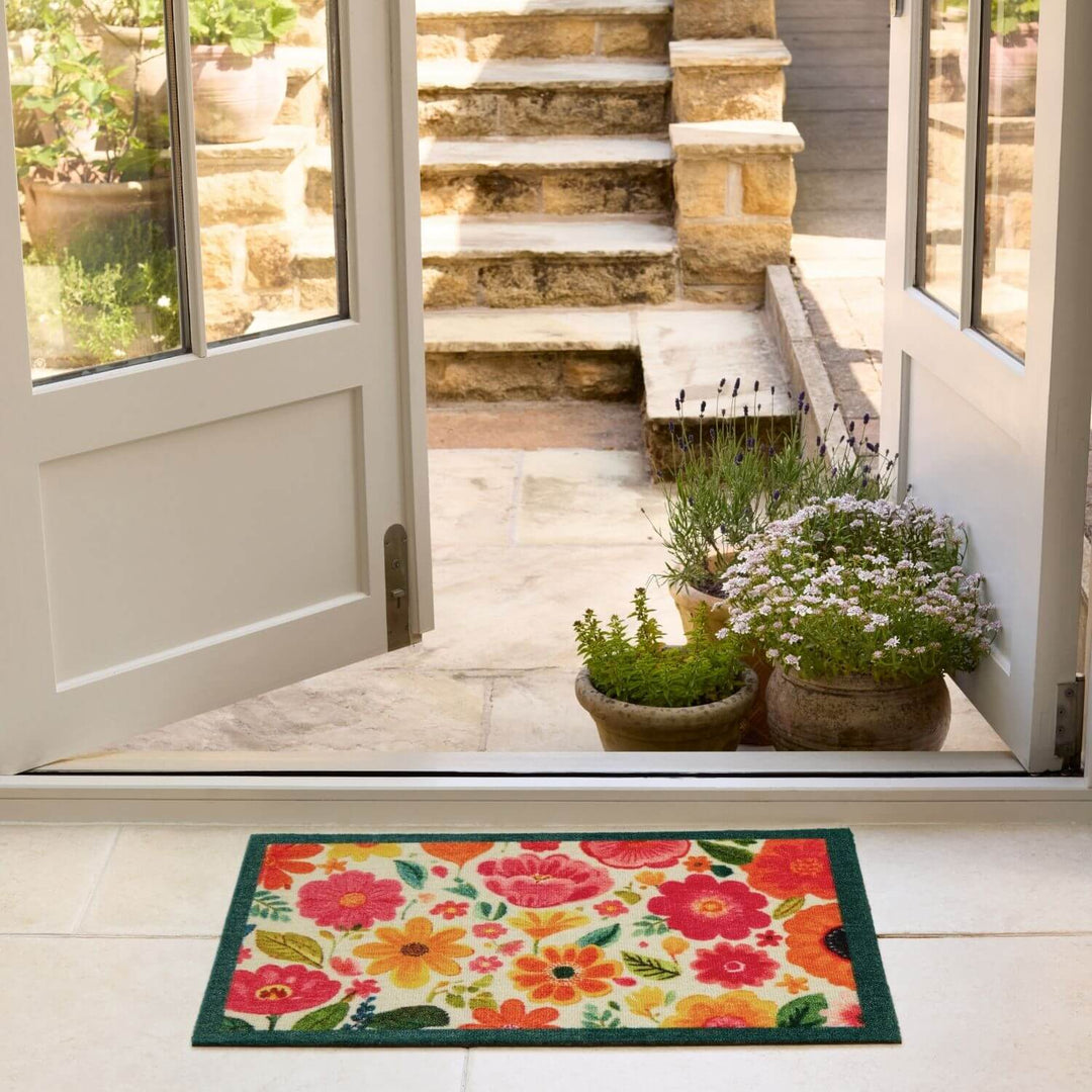 Floral doormat in front of a house with plants and steps visible