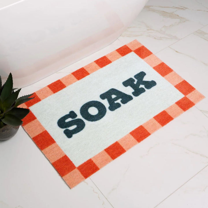Doormat with 'SOAK' text on a checkered border in a bathroom setting