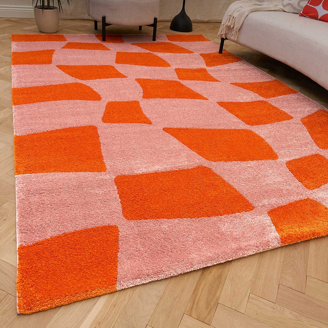 Geometric patterned rug with orange and pink squares on a wooden floor.
