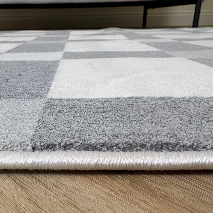 Close-up of a checkered area rug with gray, white, and beige squares on a wooden floor.