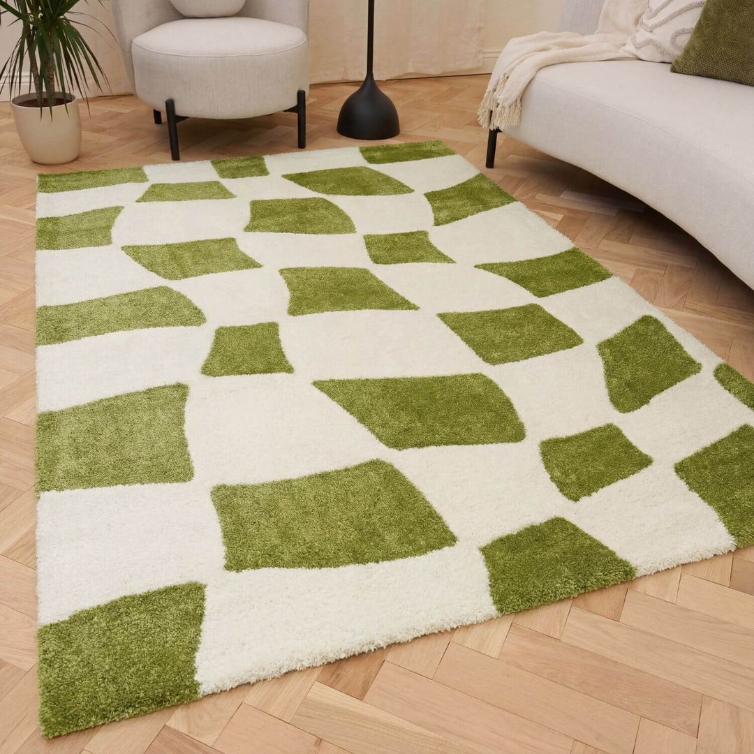 Green and white checkered rug on a wooden floor with a couch and plant in the background.